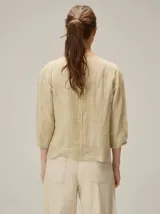 Blusa de algodón color marrón, con escote redondo, mangas tres cuartos con volumen sutil y costuras verticales decorativas en el frente.