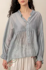 Blusa de seda gris con mangas largas abullonadas y puños con volados, escote en V con cuello fruncido y botones frontales.