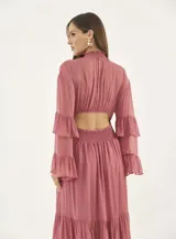 Vestido largo de gasa color rosa viejo, con cuello alto fruncido, cintura elástica tipo nido de abeja y mangas largas con volados. La falda presenta un diseño de capas con volados en el ruedo.