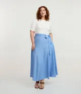 Vestido midi Ashua con parte superior blanca de manga corta y escote redondo, y pollera celeste con rayas verticales y lazo ajustable en la cintura.