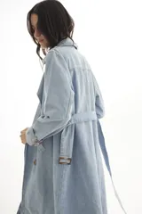 Trench de jean largo con diseño relajado, cuello solapa, cierre frontal con botones y charreteras en los hombros.