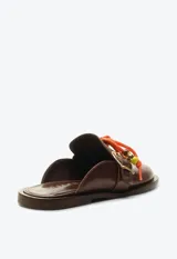 Zueco mocasín de cuero marrón, con taco plano, hebilla metálica dorada lateral y detalle de cordón naranja con cuentas decorativas en el empeine.