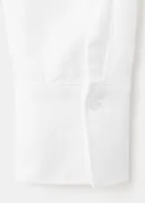Camisa de lino blanca de corte recto, con cuello camisero, mangas largas y cierre frontal oculto de botones.