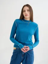 Polera de cuello alto confeccionada en tela rib color azul, con mangas largas y hombreras. Presenta costuras decorativas con pespuntes en hilo de color contrastante en el cuello, hombros y puños.