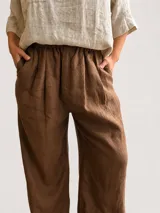 Pantalón palazzo blanco de lino, con cintura elástica fruncida y botón frontal decorativo. Presenta un corte amplio y relajado de pierna ancha.