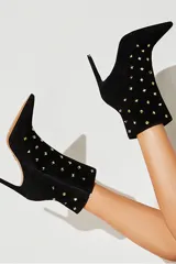 Botineta negra de gamuza con punta fina, taco aguja y apliques de tachas doradas.