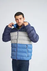 Campera puffer con diseño color block en tonos azul marino, gris y azul claro. Cuenta con capucha, cierre frontal completo, bolsillos laterales con cierre y logo estampado en el pecho.