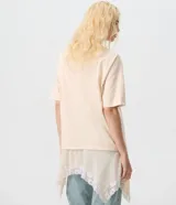 Remera oversized de algodón color beige, de manga corta y cuello redondo, con superposición inferior liviana, bajo asimétrico y aplicación de encaje.