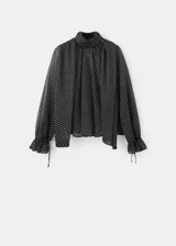 Blusa de poliéster color negro con estampado de lunares blancos, cuello alto con detalle de lazo, manga larga con puños elásticos y diseño recto.