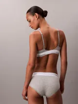 Bralette de triángulo Calvin Klein, confeccionado en una mezcla de algodón y modal. Presenta copas ligeramente forradas sin aros, tirantes ajustables y la icónica banda elástica con el logo de la marca en contraste.