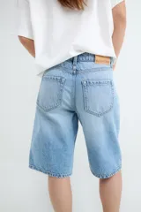 Bermuda de denim celeste, confeccionada en algodón con diseño de tiro medio, bolsillos traseros aplicados y parche de cuero sintético con marca en la pretina.