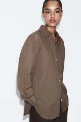 Camisa oversize de algodón con cuello solapa, manga larga y cierre frontal con botones. Presenta un bolsillo de plastrón en el frente y un diseño de corte amplio con ruedo redondeado.