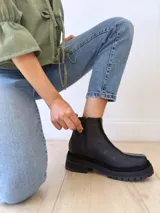 Botas negras de cuero con caña baja, cierre lateral con cremallera y suela track.