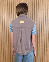 Chaleco de denim azul oscuro con diseño a rayas verticales, cuello camisero, cierre frontal con botones y bolsillos frontales con detalles de costuras bordadas en color blanco en los bordes y sisas.