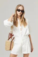 Short de lino blanco con cintura alta, tablas, bolsillos laterales y cierre frontal con gancho metálico.