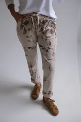 Pantalón de corte recto y ajuste holgado, confeccionado en tela beige con estampado floral en tonos marrones. Presenta cintura elástica con cordón ajustable y ruedos doblados.