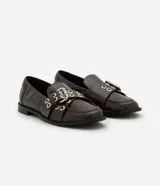 Mocasín Satinato de poliuretano color marrón oscuro, con punta redondeada, tacón bajo y empeine decorado con tiras cruzadas, hebilla ajustable y ojetes metálicos.