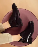 Botinetas negras con suela track, combinando cuero texturizado en la parte frontal y cuero charolado en la parte trasera. Diseño de caña baja con detalle de corte lateral.