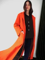 Tapado largo de paño color naranja, con solapas clásicas, bolsillos frontales y detalles en cuero. Presenta un diseño estructurado y elegante con forro parcial.