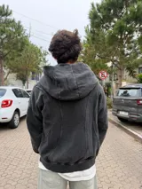 Campera con capucha y cierre frontal, de corte oversize y acabado acid wash en color gris oscuro. Presenta costuras curvas decorativas en el frente y puños acanalados.