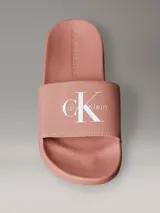 Ojotas tipo slide Calvin Klein Jeans, color rosado, con banda superior de lona de algodón reciclado y logo de la marca estampado en blanco. Presentan suela de EVA con plantilla ergonómica moldeada.