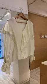Blusa de color marrón con escote en V, mangas largas abullonadas con puños elásticos y detalles de volados en los hombros y el frente.