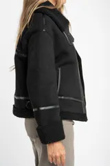 Campera tipo gamulán color negro, con interior y detalles en cuello y puños de corderito sintético. Presenta cierre frontal, detalles en cuero sintético y corte oversize.