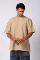 Remera de corte oversized en color marrón, confeccionada en tejido de algodón con textura de micropanal. Presenta cuello redondo con detalle de costura en forma de X y mangas cortas de estilo caído.