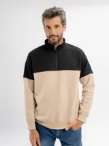 Buzo de felpa con diseño color block, combinando negro en la parte superior y beige en la parte inferior. Presenta cuello alto con cierre frontal parcial y puños elásticos.