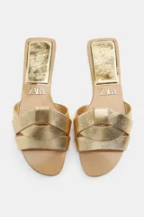 Sandalia plana dorada de piel con tiras cruzadas en la parte delantera.