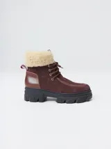 Borcegos de caña baja con diseño robusto, confeccionados en una combinación de gamuza y cuero sintético en tonos verde oliva. Presentan suela track de goma dentada en color suela, cordones al tono con ojalillos amarillos y cuello acolchado para mayor confort.