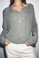 Jersey de punto color gris, con cuello redondo y abertura frontal con botones. Presenta mangas largas raglán y puños y bajo acanalados.