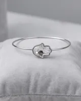 Esclava rígida de metal plateado con diseño de mano de Hamsa, decorada con un cristal facetado central.
