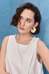 Top blanco sin mangas, con cuello redondo, diseño cruzado en el frente y cierre con botones en el hombro.
