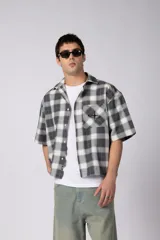 Camisa de manga corta de popelina cuadrillé en tonos gris y blanco, con corte boxy, cuello camisero, bolsillo frontal con detalle bordado y cierre frontal con botones.
