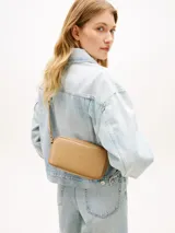 Cartera bandolera de poliuretano color beige, modelo Essential de Tommy Hilfiger, con diseño compacto de líneas redondeadas, cierre de cremallera e inscripción de la marca en bajo relieve en el frente. Cuenta con una correa cruzada ajustable de jacquard tonal.
