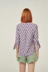 Blusa de viscosa con estampado geométrico en tonos violeta y beige. Tiene cuello mao, botones frontales y mangas 3/4 con lazo en los puños.