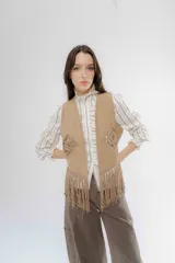 Chaleco de gamuza sintética color beige, con detalles de tejido crochet en el frente y flecos en el ruedo.