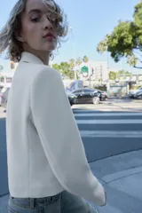 Blazer corto blanco de cuello solapa y manga larga con hombreras. Presenta un cierre frontal cruzado con dos botones dorados.