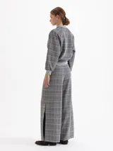 Pantalón de tiro alto con corte amplio y relajado, confeccionado en tejido de punto con estampado de cuadros tipo príncipe de gales. Presenta cintura elástica, bolsillos laterales con broches metálicos y botamangas amplias.