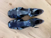 Sandalia tipo pescador de cuero charolado color azul oscuro, con talón cerrado, punta redondeada y cierre con hebilla metálica en el tobillo.