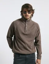 Sweater de punto color azul marino, con cuello alto, cierre frontal parcial y tapeta con botones. Presenta mangas raglán y puños y ruedo acanalados.