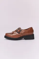 Zapato mocasín color marrón de cuero con hebilla metálica negra y detalle de flecos.
