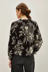 Camisa de viscosa negra con estampado floral en blanco, escote en V con lazo, cuello mao fruncido y mangas largas abullonadas con puños elásticos.