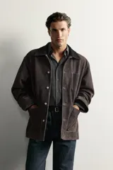 Cazadora de corte relaxed fit confeccionada en piel de ante de color marrón oscuro, con efecto lavado. Cuenta con cuello de solapa, manga larga, bolsillos frontales de parche y cierre frontal con botones.
