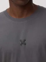 Remera de corte oversize color gris oscuro, con cuello redondo y pequeño detalle bordado en forma de cruz en el centro del pecho.