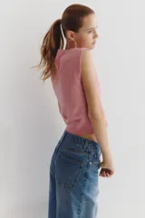 Chaleco corto de punto suave color rosado, con cuello redondo y cierre frontal de botones metálicos.