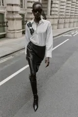 Camisa de cuello solapa y manga larga, con estampado de rayas verticales blancas y grises. Presenta dos aplicaciones de flores de encaje negro en la parte frontal. Cierre frontal con botones ocultos por solapa.