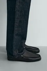 Mocasín de cuero negro, de estilo clásico y minimalista, con suela fina y horma cuadrada.