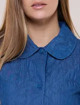 Chaqueta azul de algodón con diseño acolchado y bordado de flores, cuello redondo y cierre frontal con botones a presión metálicos. Incluye bolsillos delanteros y forro interno a tono.